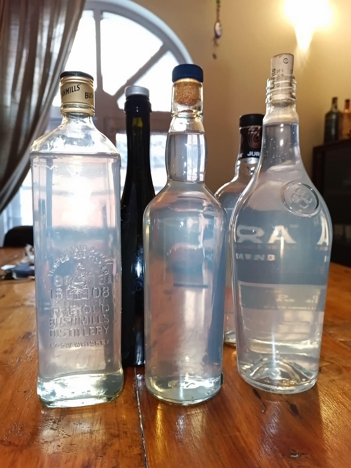Bottles of home-batch gin on a wooden table, backlit by a window